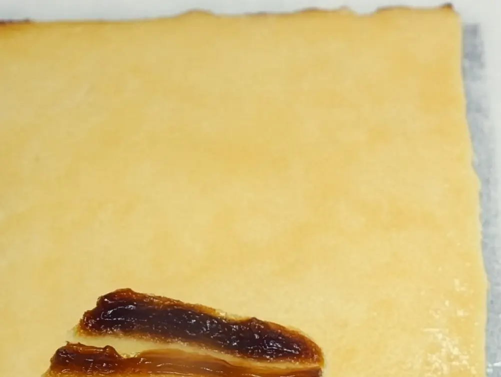 A large, light-colored sheet of pastry sits above two smaller pieces spread with a dark, sticky filling.