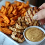 Grilled chicken pieces and sweet potato fries are served with a dipping sauce.