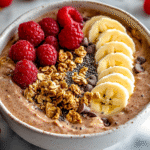 Close-up of a chocolate peanut butter Greek yogurt protein bowl with bananas, raspberries, granola, chia seeds, and chocolate chips.